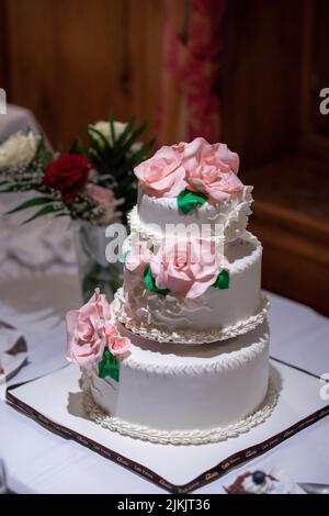 Eine vertikale Nahaufnahme der traditionellen, dreistöckigen weißen Hochzeitstorte mit rosa Rosen Stockfoto