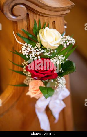 Eine vertikale Aufnahme von Blumenschmuck auf einer Holzbank in der Kirche während einer Hochzeitszeremonie Stockfoto