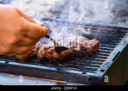 Preparing meat rolls called mici or mititei on barbecue. close up of grill with burning fire with flame and smoke. Stock Photo