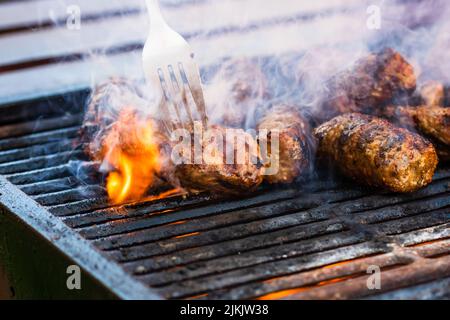 Preparing meat rolls called mici or mititei on barbecue. close up of grill with burning fire with flame and smoke. Stock Photo