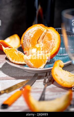 Eine Nahaufnahme aus halbgeschälter Orange mit Scheiben und einem Messer auf einem Teller auf einem Tisch Stockfoto