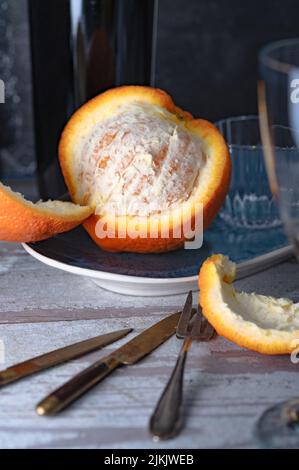 Eine Nahaufnahme aus halbgeschälter Orange mit Scheiben und einem Messer auf einem Teller auf einem Tisch Stockfoto