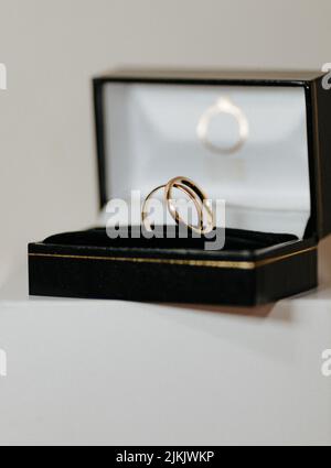 Eine vertikale Nahaufnahme von zwei Eheringen in einer schwarzen Geschenkbox vor grauem Hintergrund Stockfoto