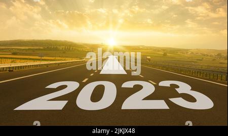 Konzept für das neue Jahr 2023. Text 2023 geschrieben auf der Straße in der Mitte der Asphaltstraße bei Sonnenaufgang. Stockfoto