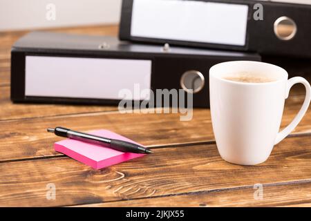 Ein Schreibtisch mit Ordnern, Haftnotizen, Stift und einer Tasse Kaffee Stockfoto