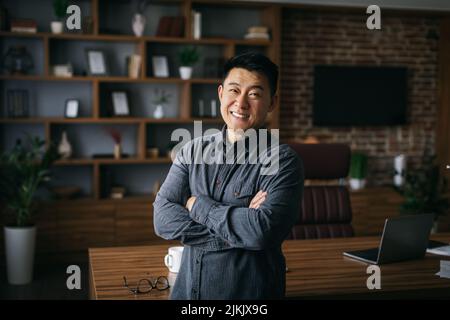 Glücklich selbstbewusst gut aussehend reifen japanischen Geschäftsmann mit gekreuzten Armen auf der Brust in dunklen Schrank Stockfoto