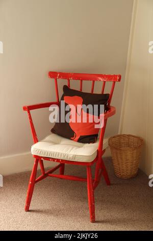 Eine vertikale Aufnahme eines roten Stuhls mit einem Kissen in der Ecke des Hauses Stockfoto