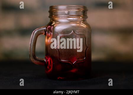 Eine Nahaufnahme eines leeren Farbglasgefäßes mit Farbverlauf und einem Griff auf einem Tisch Stockfoto