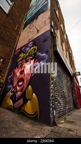 Ein niedriger Graffiti-Winkel eines rauchenden Mannes an der Wand eines alten Gebäudes in London Town Stockfoto