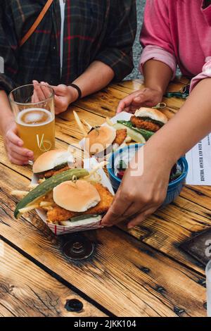 Zwei Frauen an einem Tisch im Freien mit breitem Essen in der Brauerei von Sliders Sandwiches, Pommes frites, Gurke, Salat, Bier, Menü Stockfoto