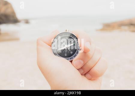 Nahaufnahme, Hand mit analogem Kompass am Strand vor dem Meer, Konzeptreise, Sommer, selektiver Fokus. Stockfoto