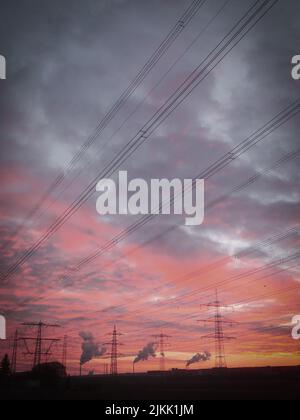 Die Stromleitungen und elektrischen Masten gegen einen bewölkten Sonnenuntergang Himmel Stockfoto