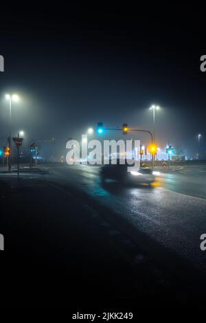 Eine Vertikale eines Autos, das in einer leeren Straße fährt, beleuchtet mit Laternen in der Nacht, aufgenommen in Langzeitbelichtung Stockfoto