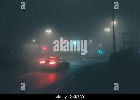 Ein Blick auf ein Auto, das in einer leeren Straße fährt, die nachts mit Laternen beleuchtet ist, aufgenommen bei langer Belichtung Stockfoto