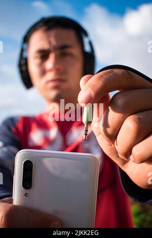 Eine vertikale Aufnahme eines Mannes, der Kopfhörer mit einem Telefon verbindet Stockfoto