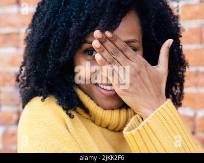 Eine Afrikanerin aus Spanien in einem gelben Pullover, der ihr Gesicht mit einer Hand bedeckt Stockfoto