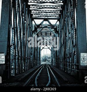 Eine Graustufenaufnahme der Eisenbahnbrücke mit Warnschildern am Eingang tagsüber Stockfoto