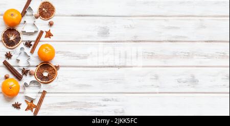 Würziger weihnachtlicher Hintergrund. Kandierte Orange, Zimtstangen, Sternanise, Weihnachtsformen für Gebäck, Nüsse und Mandarinen auf einem weißen Holztisch. Anzeigen Stockfoto