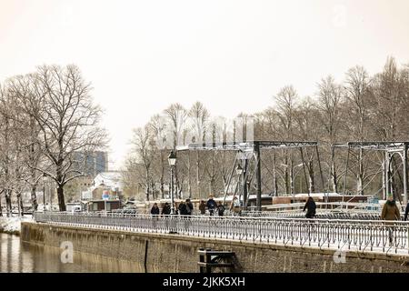 Straßenszene mit Menschen, die im Winter am Leidsche Rijn Kanal entlang der Schleusentor-Boulevard in Utrecht mit einer Stahlbrücke im Hintergrund spazieren Stockfoto