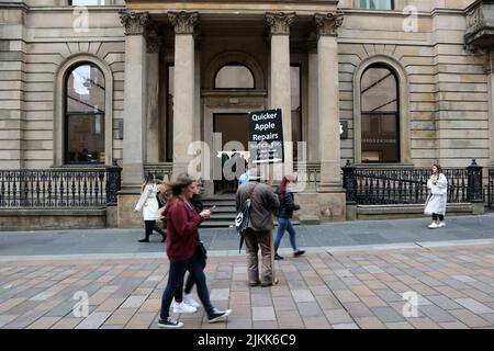 Buchanan Street, Glasgow, Schottland, Großbritannien. Ein Mann steht vor dem Apple-Einzelhandelsgeschäft mit einem Plakat, das billigere Apple-Reparaturen wirbt Stockfoto