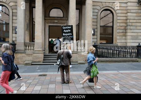 Buchanan Street, Glasgow, Schottland, Großbritannien. Ein Mann steht vor dem Apple-Einzelhandelsgeschäft mit einem Plakat, das billigere Apple-Reparaturen wirbt Stockfoto