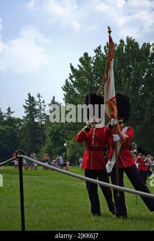 Eine vertikale Aufnahme von zwei königlichen Führern, die eine Flagge halten und auf einem grünen Gras in einem Park in Kanada stehen Stockfoto