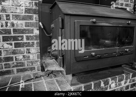 Eine Graustufenaufnahme eines alten Holzofens in einem Backsteinhaus Stockfoto