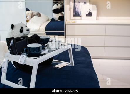 Moskau, Russland, September 2019:IKEA Showroom: Das Schlafzimmer ist weiß mit blauen Akzenten. Panda sitzt auf dem Bett an einem tragbaren Tisch mit Tassen und Schüsseln, el Stockfoto