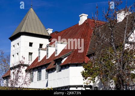 Eine Nahaufnahme eines weißen holländischen Gebäudes mit den roten Dachziegeln hinter den blattlosen Ästen von Bäumen Stockfoto