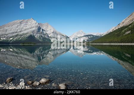 Eine malerische Aussicht auf einen See, der felsige Berge reflektiert, die mit grünen Pinien an einem sonnigen Tag bedeckt sind Stockfoto