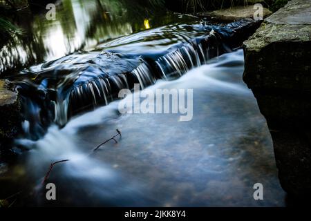 Nahaufnahme eines kleinen Wasserfalls, der flussabwärts in einen Wald fließt, mit langer Belichtung Stockfoto