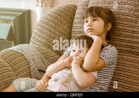 Eine wunderschöne Aufnahme einer älteren Schwester, die ihre kleine Schwester umarmte und gemeinsam einen Fernseher ansah Stockfoto