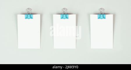 Leere weiße Papiere mit einer Büroklammer auf grauem Hintergrund, Platz für Text, Erinnerung oder Nachricht im Büro, Kommunikationskonzept Stockfoto