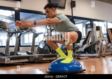Porträt eines kaukasischen Mannes im Fitnessstudio, der Übungen auf einem Gummiball macht, gesundes und gesundes Leben beim Sport Stockfoto