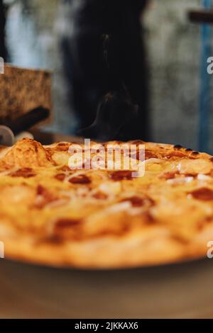 Eine frisch gebackene, heiß dampfende, leckere Pizza mit Käse und Wurst auf einem Tisch Stockfoto