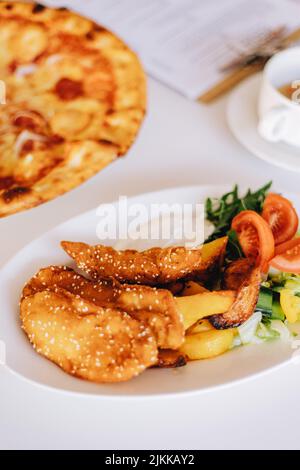 Eine frisch gebackene leckere Pizza mit Käse und Wurst und Chicken Nuggets mit Gemüse auf einem Tisch Stockfoto