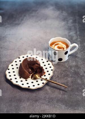 Eine vertikale Aufnahme eines süßen Lavakuchens aus Schokolade auf dem gepunkteten Teller mit einer Tasse Milchkaffee Stockfoto