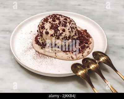 Eine Nahaufnahme einer Portion köstlicher, süßer Tiramisu-Torte mit drei Löffeln auf dem weißen Teller Stockfoto
