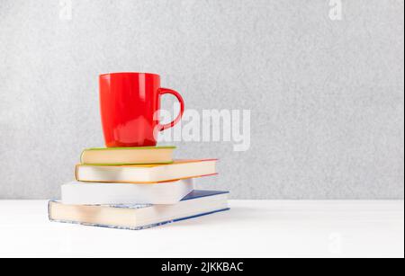 Bücher mit roter Tasse auf einem Tisch mit grauem Hintergrund und Copyspace Stockfoto