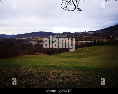 Der wolkige Himmel über dem grünen Feld mit einer Herde von Schafen und Dorfhäusern, die weit entfernt zu sehen sind Stockfoto