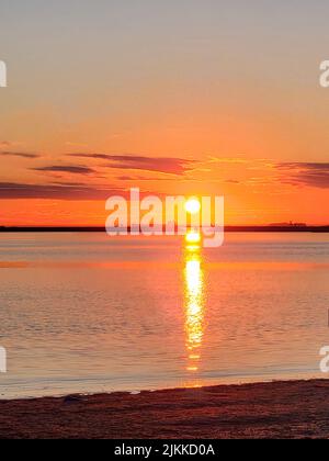 Eine vertikale Aufnahme des Ozeans während des Sonnenaufgangs vom Strand. Stockfoto