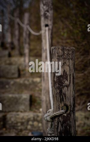 Eine vertikale Aufnahme eines hölzernen Zaunpfosten mit Seil auf einem verschwommenen Hintergrund Stockfoto