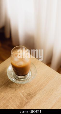 Eine Draufsicht auf eine eisgekühlte Kaffeebecher-Tasse auf einem Holztisch mit Vorhängen im Hintergrund zu Hause Stockfoto