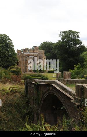 Eine vertikale Aufnahme des Steinhawarden Castle durch eine Brücke in Hawarden, Flintshire, Wales mit Bäumen und einem grau bewölkten Himmel Stockfoto