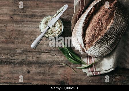 Blick von oben auf frisch gebackenen Laib Brot auf Holztisch mit Glas Schmalz und Handtuch in der hellen Küche platziert Stockfoto