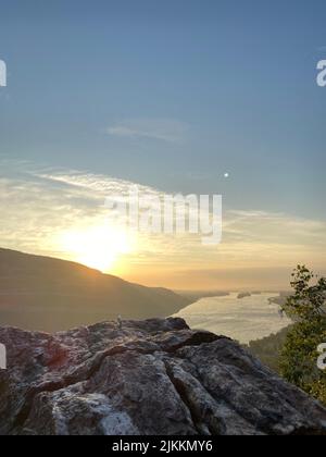 Eine vertikale Aufnahme einer Klippe am Rheinufer und grünen Bergen bei Sonnenuntergang in Deutschland Stockfoto