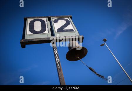 Eine Aufnahme einer alten Flip-Uhr auf einem Metallmast und einer großen Metallglocke, die daran hängt Stockfoto