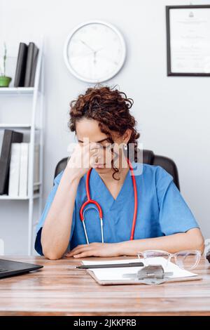 lateinamerikanische Ärztin in ihrem Büro müde und gestresst, ausgebrannte Konzept. Stockfoto