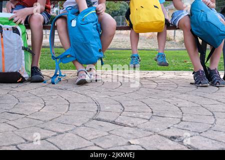 Beschnittenes Bild von Schulkindern, die mit ihren Rucksäcken auf einer Bank sitzen. Stockfoto