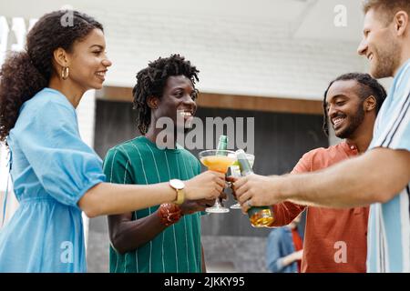 Eine vielfältige Gruppe junger Menschen, die auf der Terrassenparty Getränke genießen und mit Gläsern toasten Stockfoto
